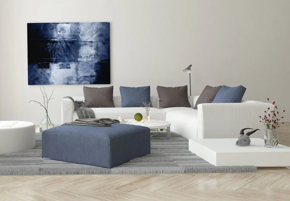 White couch on a grey rug next to a blue ottomon and a blue canvas. 