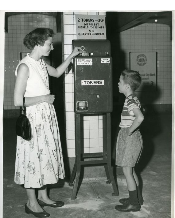 A woman and a child stand in front of a machine that distributes metro tokens.