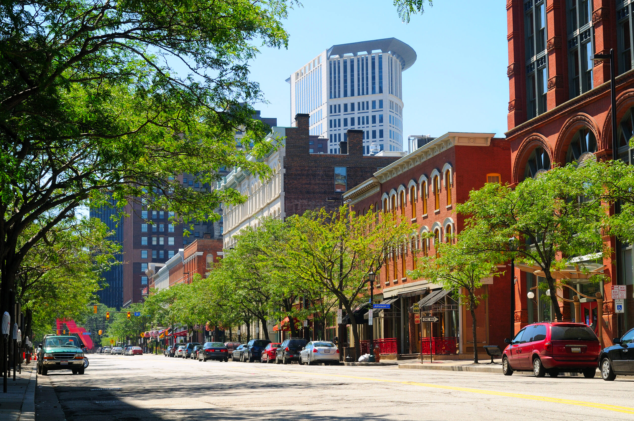 The city streets of Cleveland, OH on a sunny day with green, leafy trees dotting the sidewalks.