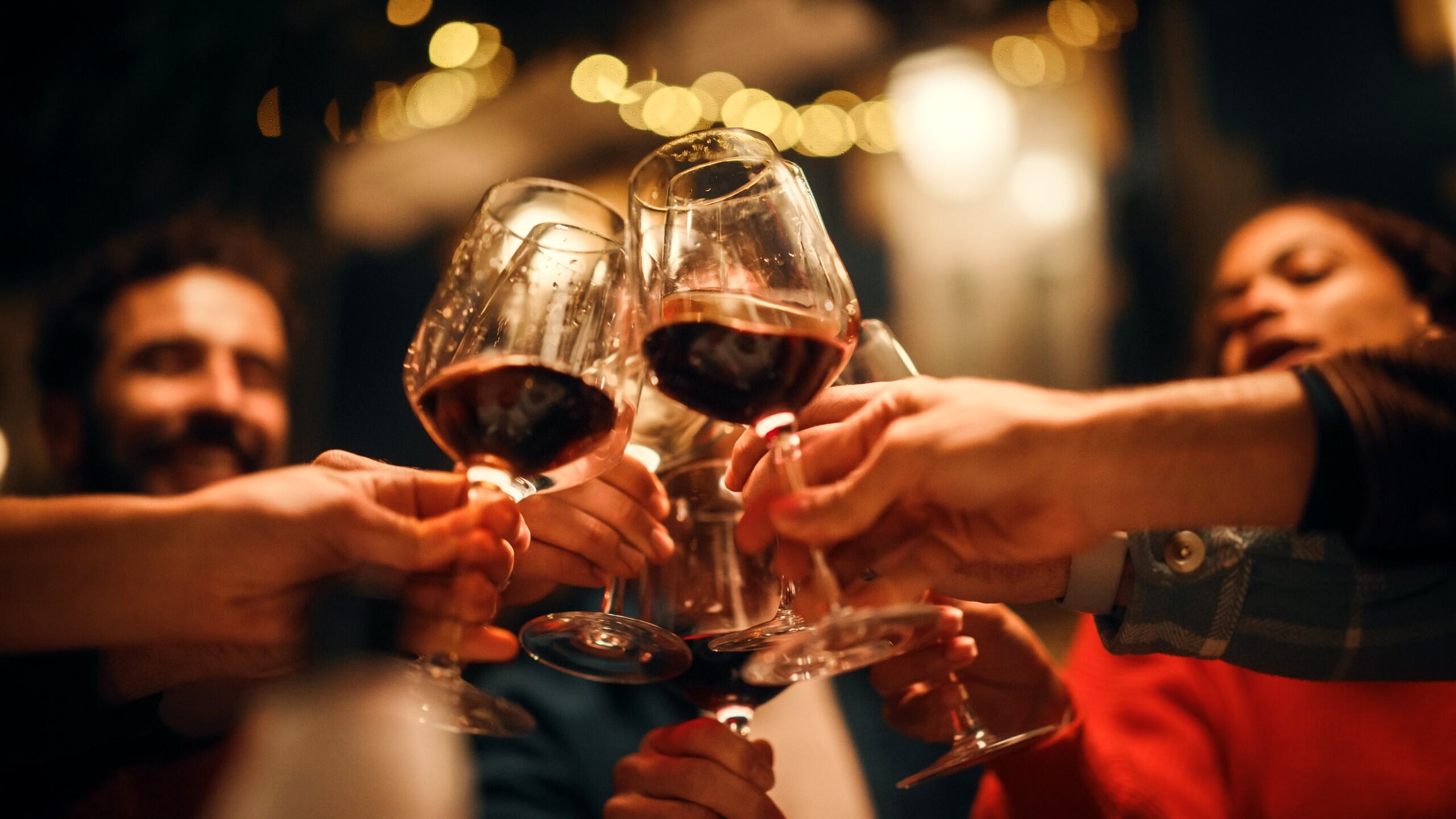 A group of people toast wine glasses full of red wine.