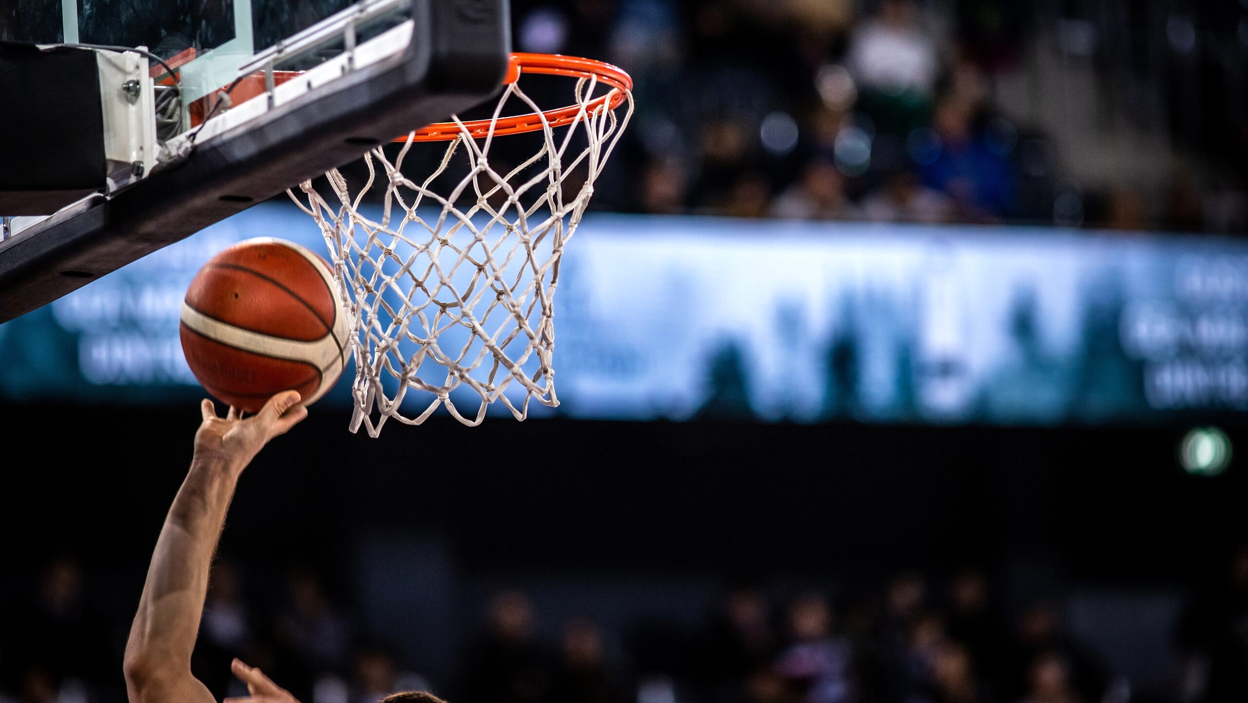 A basketball player reaches up to dunk a basketball into a hoop.