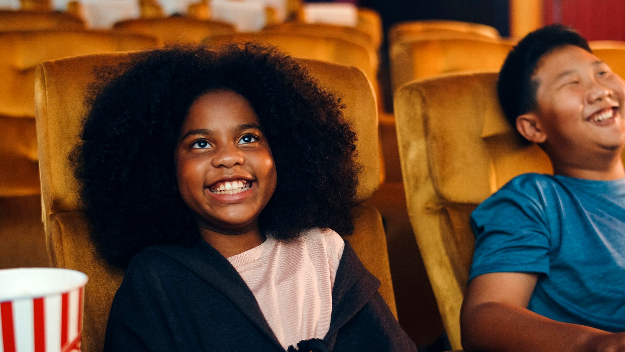 Two young children sit in theatre seats enjoying a performance.