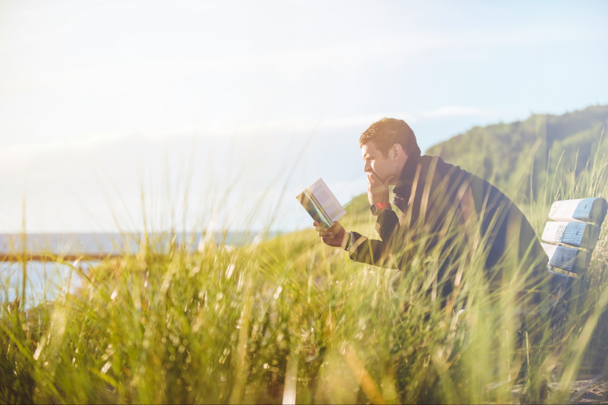 A man relaxing outside, reading a book on a bench.