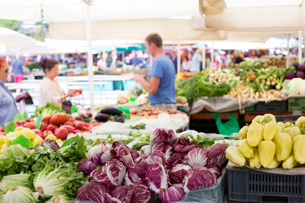 People shopping in a farmers' market with fresh produce in the foreground.