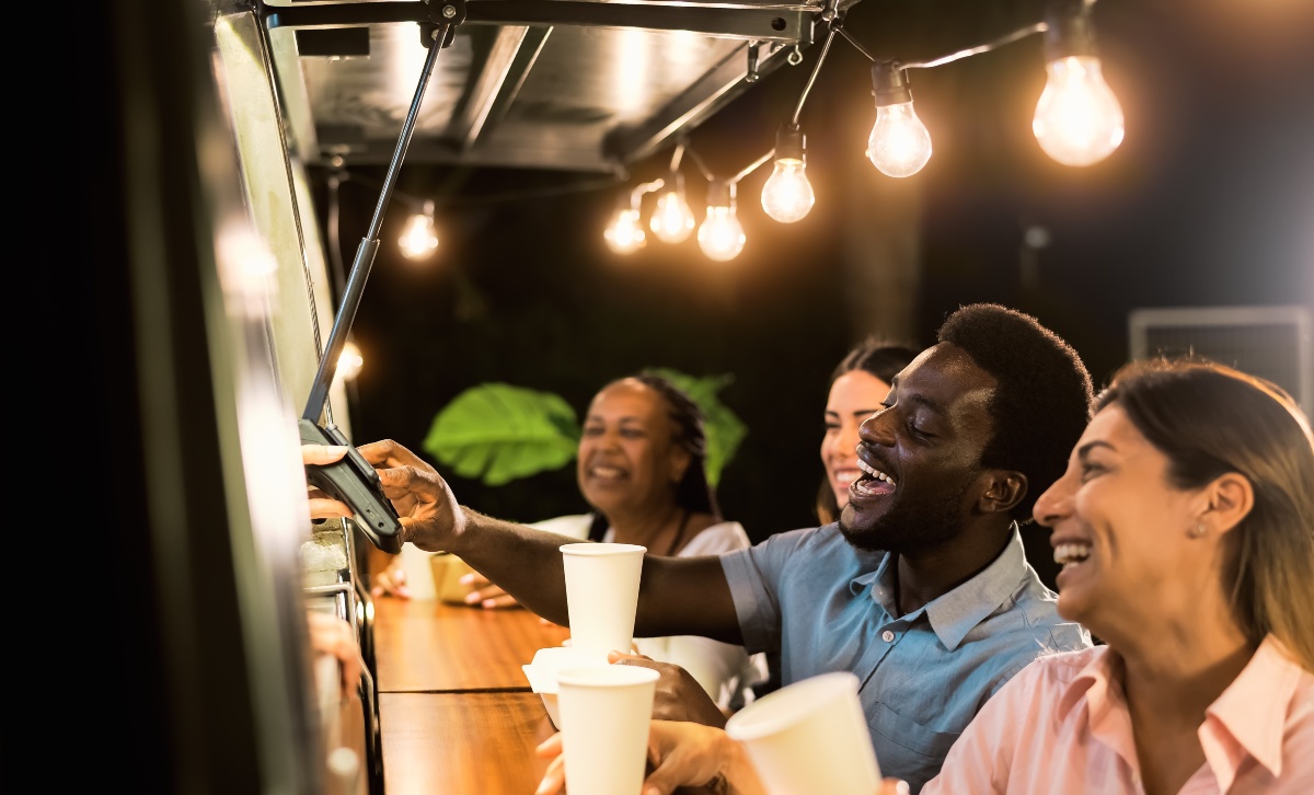 A few people standing at a food truck with white drink cups laughing and smiling.