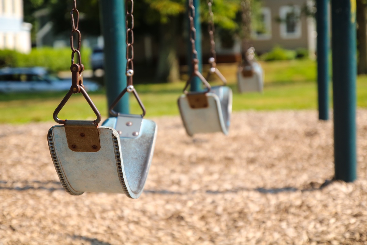 A close up of an empty swing set on a bark playground. 