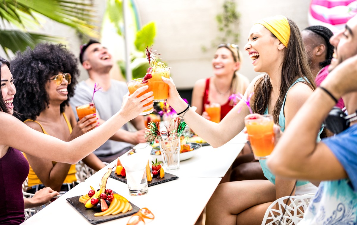 Un grand groupe d'amis est assis à une table en plein air et toaste les boissons sur le thème de l'été lors de leur réunion d'été.